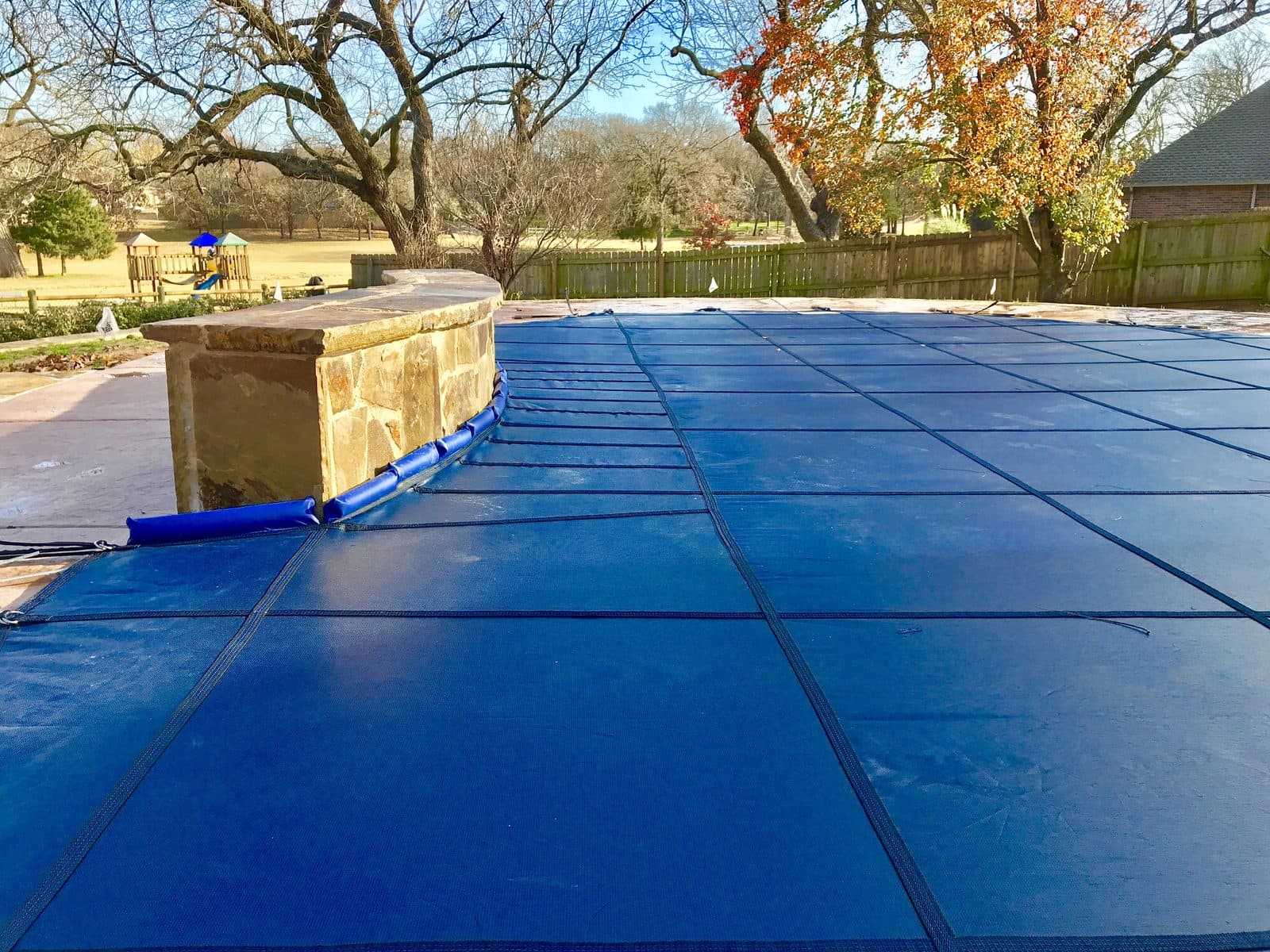 Close-up of a blue inground pool safety cover anchored along a raised stone wall
