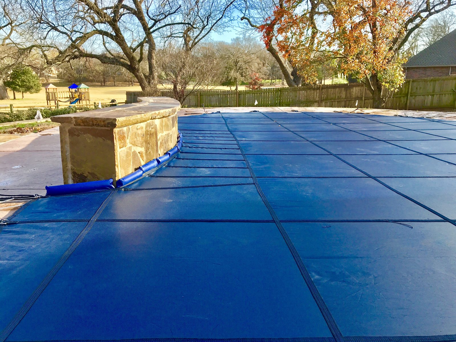Blue inground pool safety cover anchored along a raised stone wall