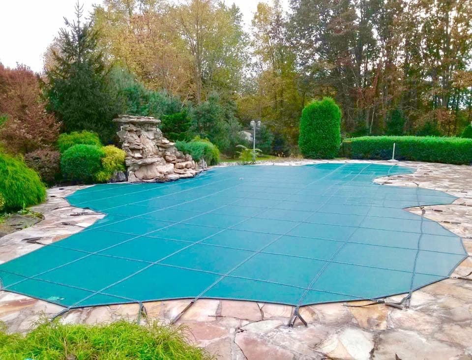 Safety cover fitted to a freeform Oklahoma pool with a stone waterfall